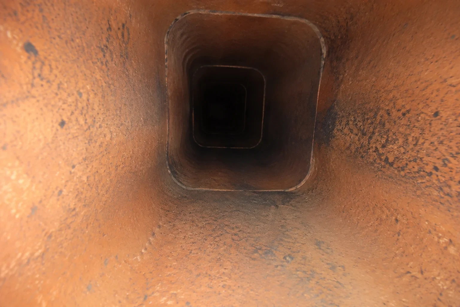 Illustration: Interior view of a rectangular terracotta flue with rounded corners and dark surface marks.