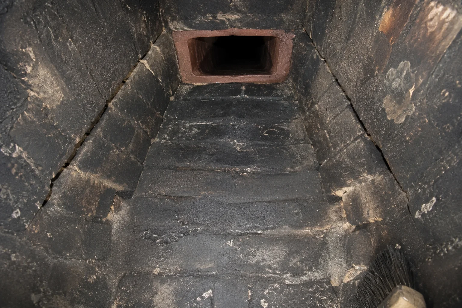 Illustration: Soot-darkened tapered masonry chamber leading to a terracotta flue opening.